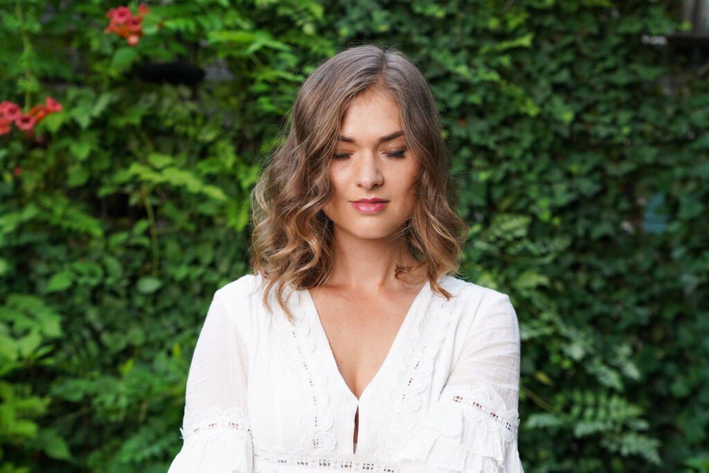 woman in white blouse against leafy backdrop