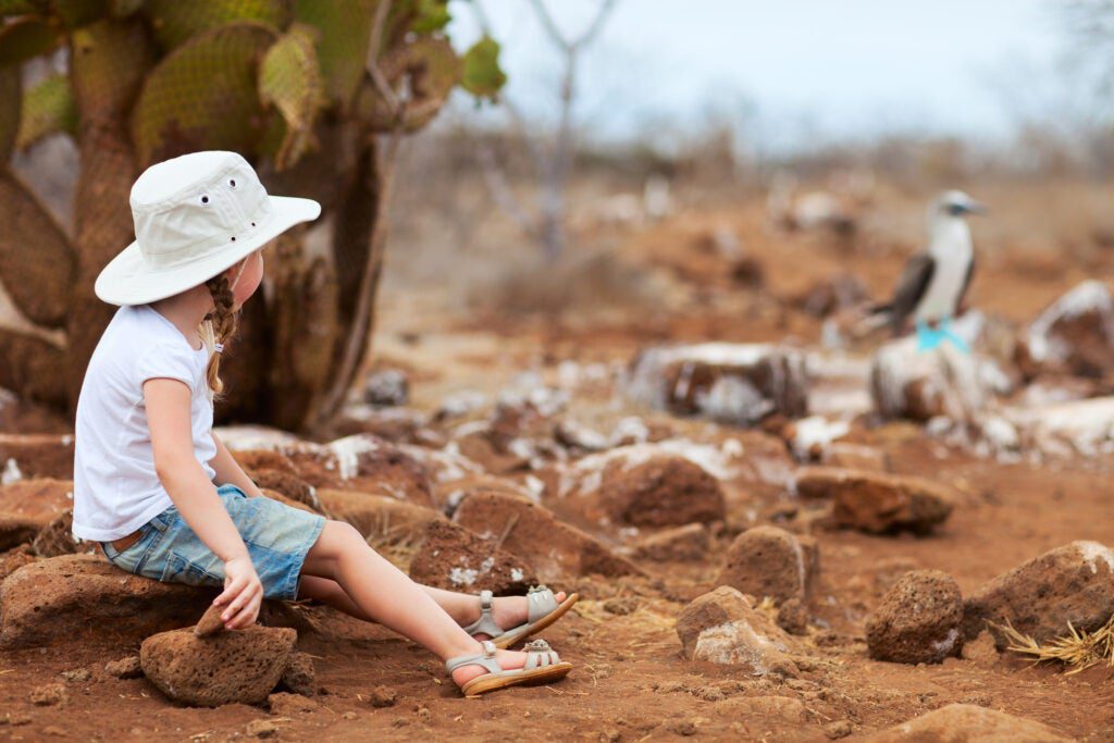 A little girl looks at a blue-footed booby in the GalÃ¡pagos.