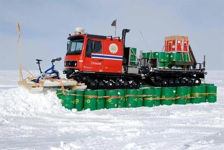 To avoid getting buried in snow drift during the Antarctic winter, the "Chinook" vehicle is placed on top of empty fuel drums in preparation for over-wintering at Camp Winter. The team consulted with meteorologists at the South Pole to determine how best to anchor and secure the equipment, sleds, and modules.