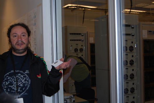 Alejandro Saez, correlator team lead for the Atacama Large Millimeter-submillimeter Array, describes the new telescope's specially built supercomputer. The telescope dishes and computer are located at 16,400 feet in the Chilean Andes, so Saez and other workers wear portable oxygen tanks.