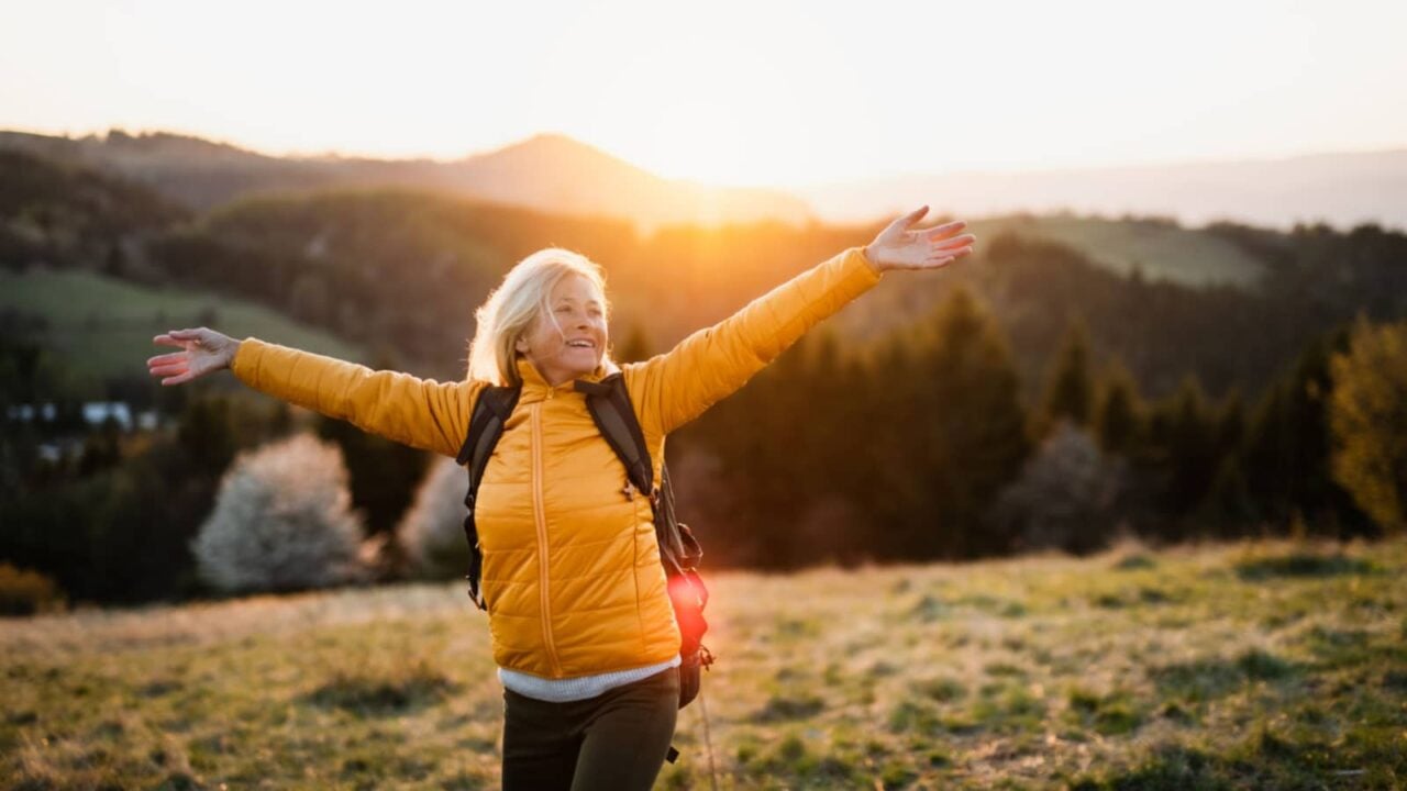 Front view of senior woman hiker standing outdoors in nature at sunset.