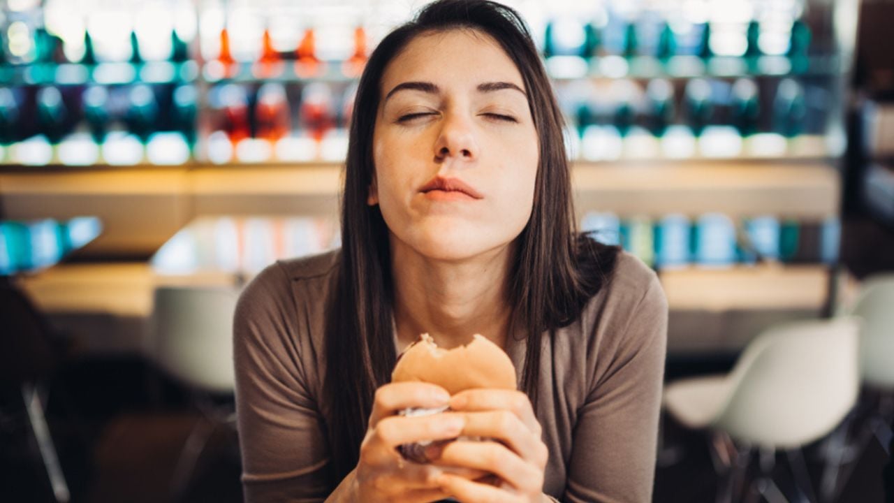 Young woman eating fatty hamburger.Craving fast food.Enjoying guilty pleasure,eating junk food.Satisfied expression.Breaking diet rules,giving up diet.Unhealthy imbalanced nutrition calorie intake.