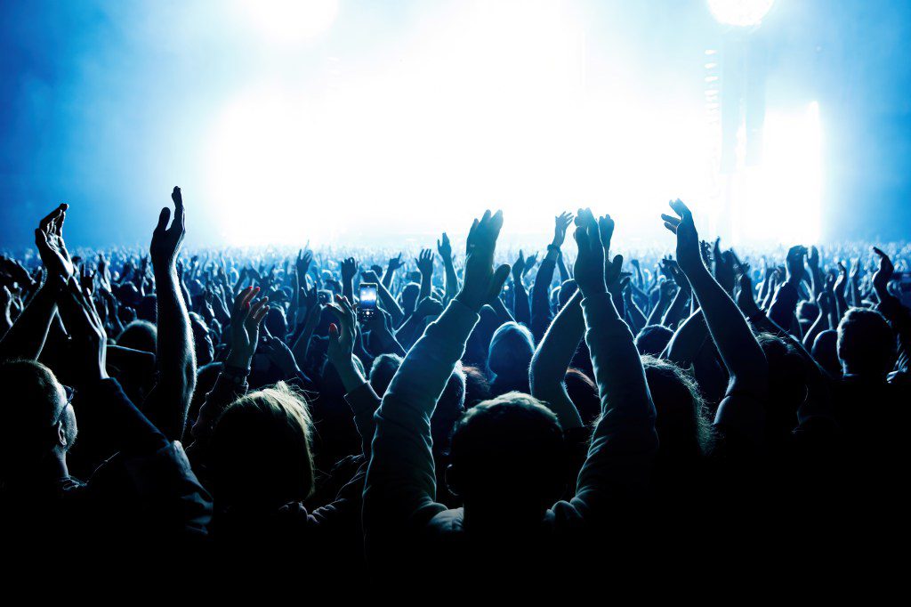 A crowd of people with raised arms during a music concert with an amazing light show. Black silhouettes