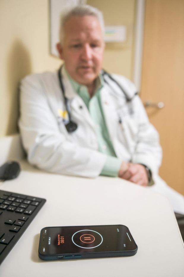 In this photo provided by University of Michigan Health-West, Dr. Lance Owens, chief medical information officer at the university, demonstrates the use of an AI tool on a smartphone in Wyoming, Mich., on Sept. 9, 2021. The software listens to a doctor-patient conversation, documents and organizes it to write a clinical note. (University of Michigan Health-West via AP)