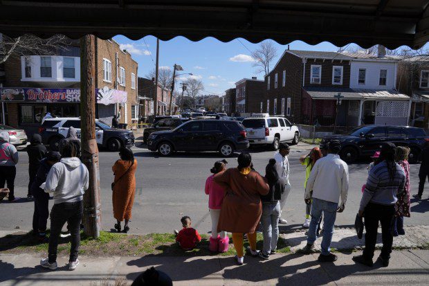 People look on as police surround a home in Trenton, N.J., Saturday, March 16, 2024. A suspect has barricaded himself in the home and was holding hostages after shooting three people to death in suburban Philadelphia. (Matt Rourke/AP)