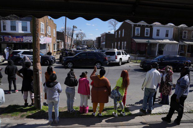 People look on as police surround a home in Trenton, N.J., Saturday, March 16, 2024. A suspect has barricaded himself in the home and was holding hostages after shooting three people to death in suburban Philadelphia. (Matt Rourke/AP)