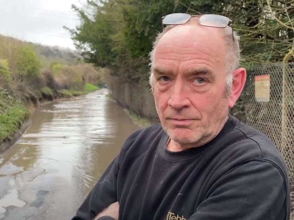 Andy Tebbutt standing on the flooded road outside his home