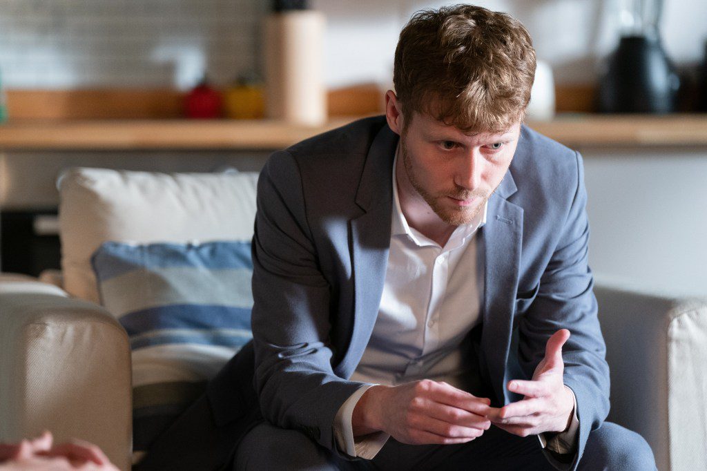 Jay sitting on a chair in the flat in EastEnders