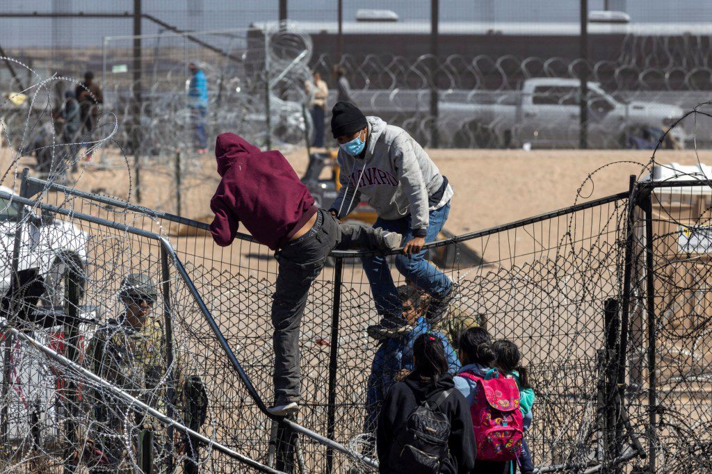 Migrants try to cross over a fence, after a group of migrants forced their way by breaking through razor wire and a fence, as SB 4 law that would empower law enforcement authorities in the state to arrest people suspected of illegally crossing the U.S.-Mexico border was temporarily blocked, as seen from Ciudad Juarez, Mexico, March 21, 2024. REUTERS/David Peinado