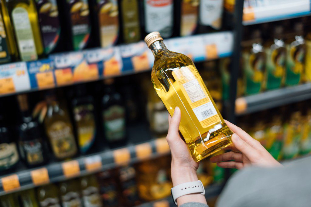 A person holds a bottle of olive oil.