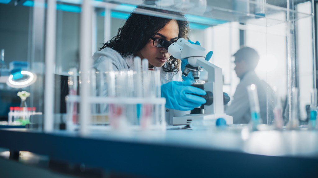 Medical Science Laboratory: Portrait of Beautiful Black Scientist Looking Under Microscope Does Analysis of Test Sample. Ambitious Young Biotechnology Specialist, working with Advanced Equipment