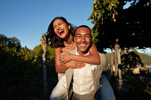 Happy groom piggybacking bride in vineyard