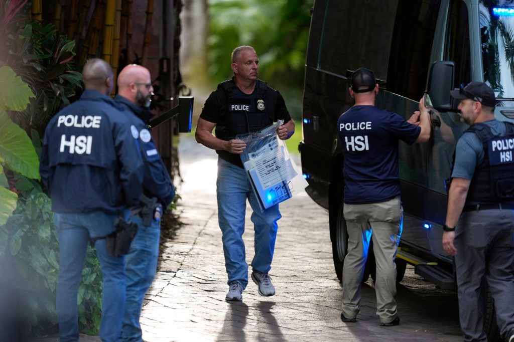 A law enforcement agent carries a bag of evidence to a van as federal agents stand at the entrance to a property belonging to rapper Sean 