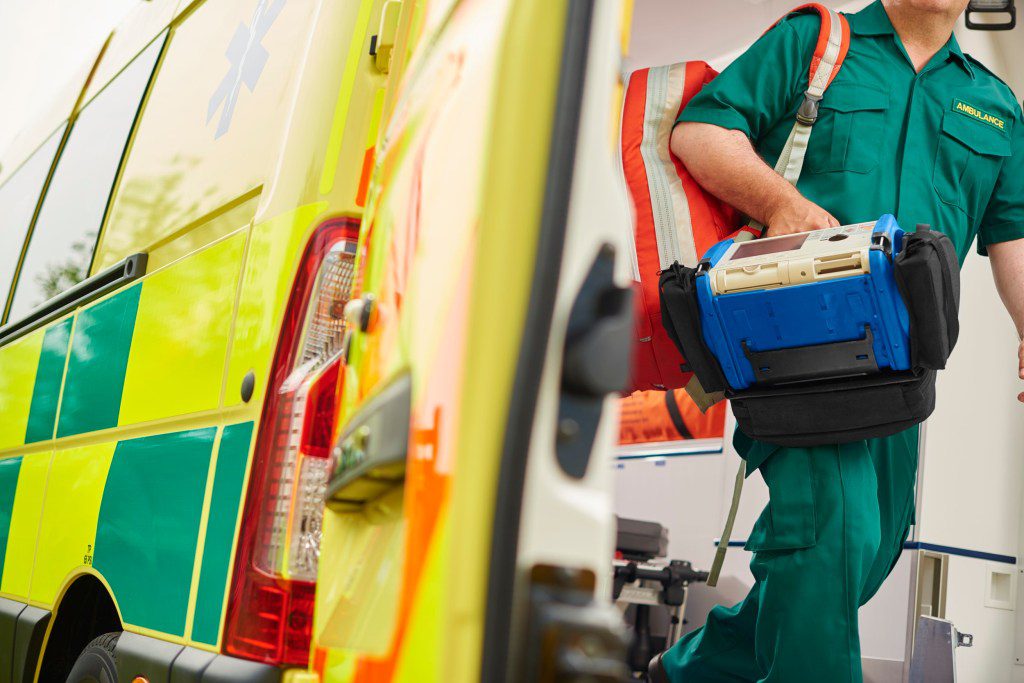 a uk ambulance staff member emerges from the back of an ambulance with his emergency backpack , and vital signs monitor .