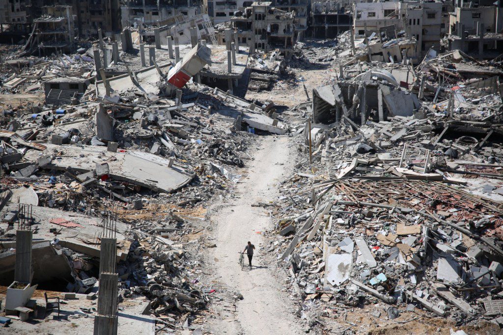 TOPSHOT - A man pushes a bycicle along as he walks amid building rubble in the devastated area around Gaza's Al-Shifa hospital on April 3, 2024, amid the ongoing conflict between Israel and the Palestinian Hamas militant group. (Photo by AFP) (Photo by -/AFP via Getty Images)